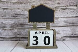 Chalkboard with April 30 date on white cube block on wooden table. photo