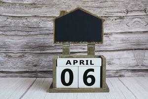 Chalkboard with April 06 date on white cube block on wooden table. photo