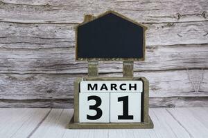 Chalkboard with March 31 date on white cube block on wooden table. photo