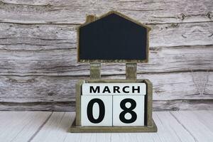 Chalkboard with March 08 date on white cube block on wooden table. photo