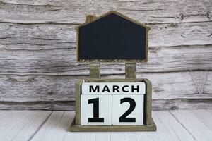 Chalkboard with March 12 date on white cube block on wooden table. photo