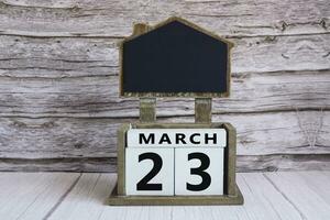 Chalkboard with March 23 date on white cube block on wooden table. photo