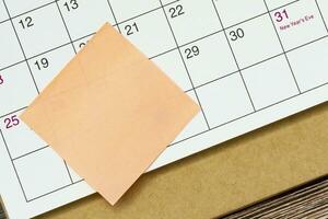 Orange paper sticky note and stuck to a calendar background. Reminder concept. photo