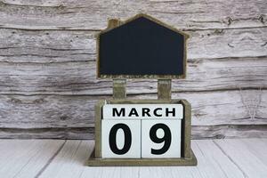 Chalkboard with March 09 date on white cube block on wooden table. photo