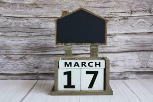 Chalkboard with March 17 date on white cube block on wooden table. photo