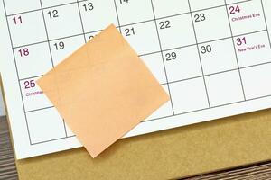 Orange paper sticky note and stuck to a calendar background. Reminder concept. photo