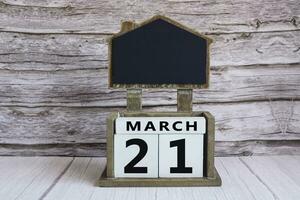 Chalkboard with March 21 date on white cube block on wooden table. photo