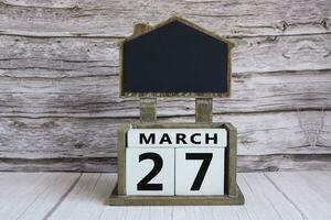 Chalkboard with March 27 date on white cube block on wooden table. photo