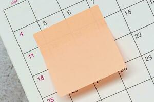 Orange paper sticky note and stuck to a calendar background. Reminder concept. photo