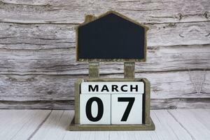 Chalkboard with March 07 date on white cube block on wooden table. photo