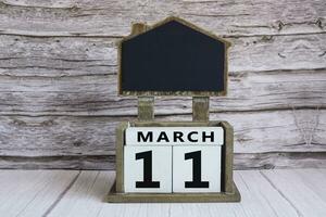 Chalkboard with March 11 date on white cube block on wooden table. photo