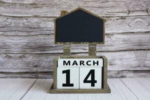 Chalkboard with March 14 date on white cube block on wooden table. photo
