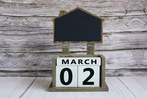 Chalkboard with March 02 date on white cube block on wooden table. photo