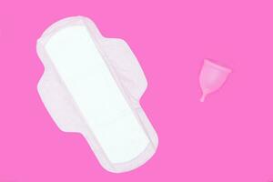 menstrual cup and regular feminine pad on a pink background, top view, copy space. Zero waste concept. Eco-friendly menstrual products photo