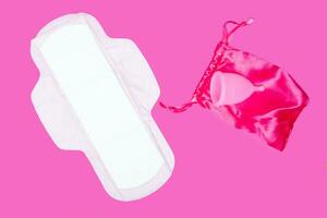 menstrual taza y regular femenino almohadilla en un rosado fondo, parte superior vista, Copiar espacio. cero residuos concepto. Respetuoso del medio ambiente menstrual productos foto