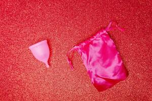 menstrual cup with satin pouch on shiny red background, top view. Zero waste concept. Eco-friendly menstrual products photo