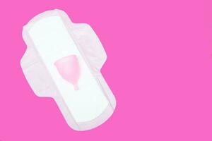 menstrual cup and regular feminine pad on a pink background, top view, copy space. Zero waste concept. Eco-friendly menstrual products photo