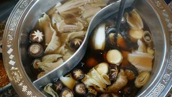 Close up of people eating together using Chopsticks putting vegetable and meat into the hotpot red spicy boiling Chinese Sichuan style soup video