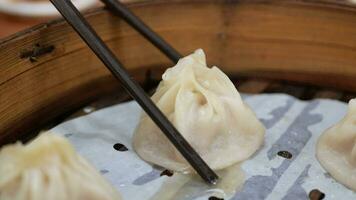 taiwanese traditional food with hot stream while using chopstick to pick up xiaolongbao from the bamboo streamer on table video