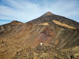 A female person sitting at the Pico Viejo mountain looking towards Mount Teide in Tenerife, Canary Islands, Spain. Famous destinations for hikers. Teide National Park, Unesco World Heritage Site. photo