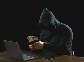 Portrait hacker spy man one person in black hoodie sitting on table looking computer laptop used login password attack security to data digital internet network system night dark background copy space photo