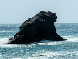 A solitary rock formation stands in the blue ocean under a clear sky, symbolizing solitude and strength. photo