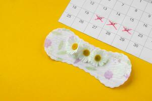 Menstrual pads with chamomiles on menstruation period calendar on yellow background. photo