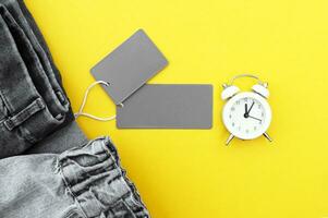 Flat lay, detail of black jeans, blank grey labels on yellow background. photo