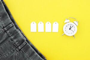 Flat lay, detail of black jeans, blank white labels on yellow background. photo