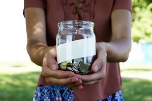 The girl is holding a glass jar with coins and a place for an inscription. photo