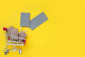 Mini shopping cart with small craft bags and empty gray tags on a yellow background. photo