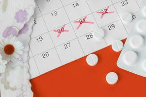 Menstrual pads and tampons on menstruation period calendar with chamomiles on red background. photo