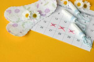 Menstrual pads and tampons on menstruation period calendar with chamomiles on yellow background. photo