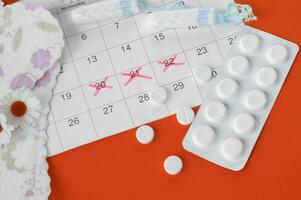 Menstrual pads and tampons on menstruation period calendar with chamomiles on red background. photo
