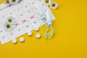 Menstrual tampons on menstruation period calendar with chamomiles on yellow background. photo