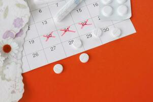 Menstrual pads and tampons on menstruation period calendar with chamomiles on red background. photo