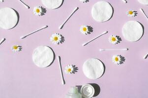 Ear sticks, white cotton pads, chamomile and tube with makeup remover on a pink background. photo