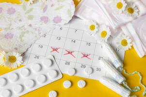 Menstrual pads and tampons on menstruation period calendar with chamomiles on yellow background. photo