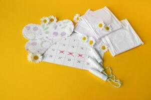 Menstrual pads and tampons on menstruation period calendar with chamomiles on yellow background. photo