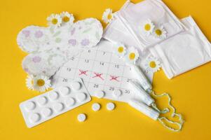 Menstrual pads and tampons on menstruation period calendar with chamomiles on yellow background. photo