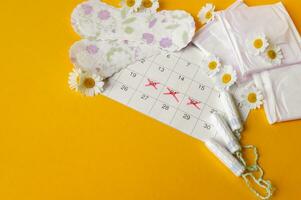 Menstrual pads and tampons on menstruation period calendar with chamomiles on yellow background. photo