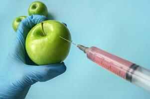 Green apple and syringe with GMO in hands on a blue background. photo