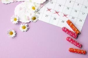 Menstrual pads and tampons on menstruation period calendar with chamomiles on pink background. photo