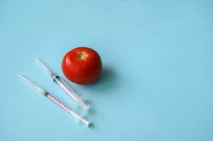 Tomato and syringe with GMO on a blue background. photo