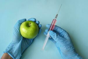 Green apple and syringe with GMO in hands on a blue background. photo
