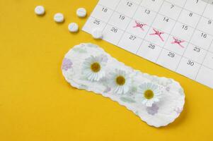 Menstrual pads with chamomiles on menstruation period calendar on yellow background. photo