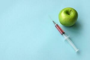 Green apple and syringe with GMO on a blue background. photo