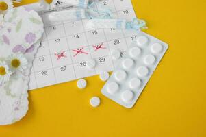 Menstrual pads and tampons on menstruation period calendar with chamomiles on yellow background. photo