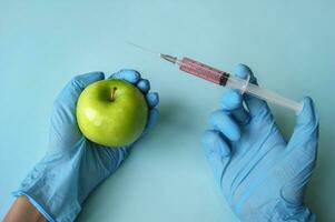 Green apple and syringe with GMO in hands on a blue background. photo