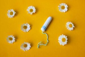 Hygienic medical female tampon with chamomiles around on a yellow background. photo